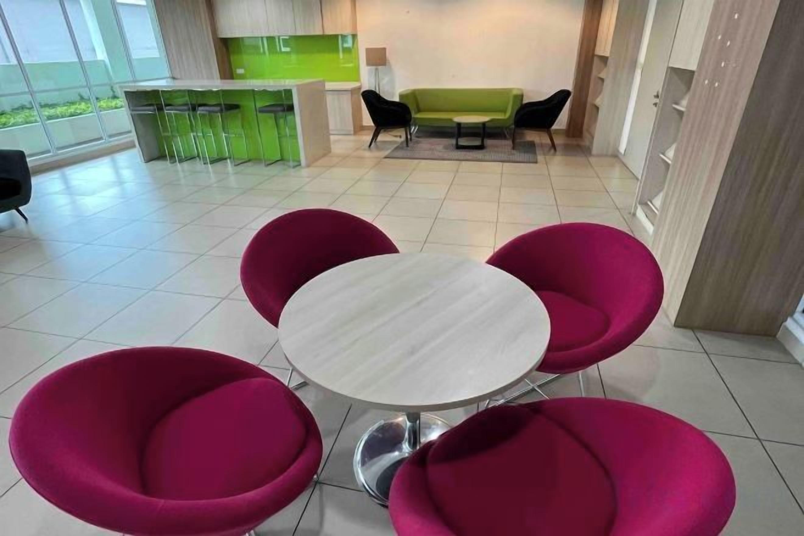Ein modernes Interieur mit einem runden Tisch, vier farbenfrohen Stühlen, einer Bar in Grün und einer Couch im Hintergrund.