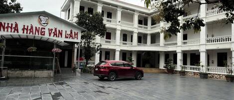 A building with a sign reading 'NHÀ HÀNG VÂN LÀM' and a red car parked in front.