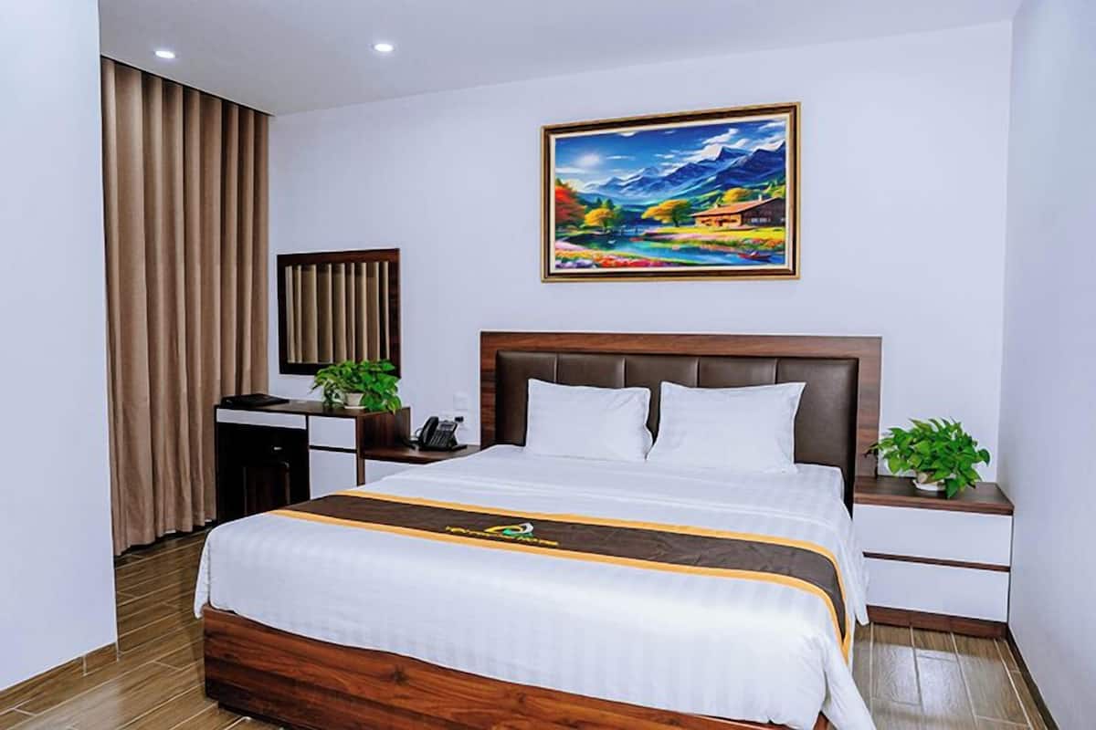 A hotel room with a large bed, a desk with a computer, a telephone, and a painting on the wall.