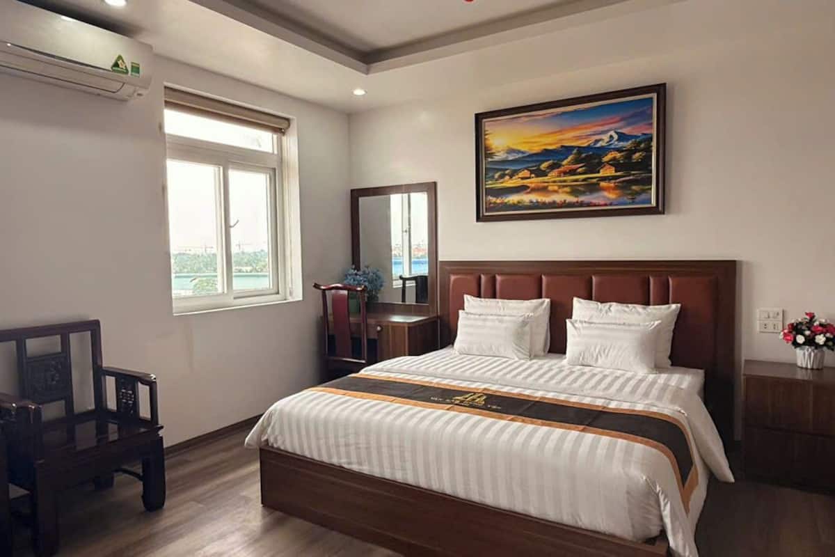 A bedroom with a bed, a desk, a chair, a window, a mirror, and a painting on the wall.
