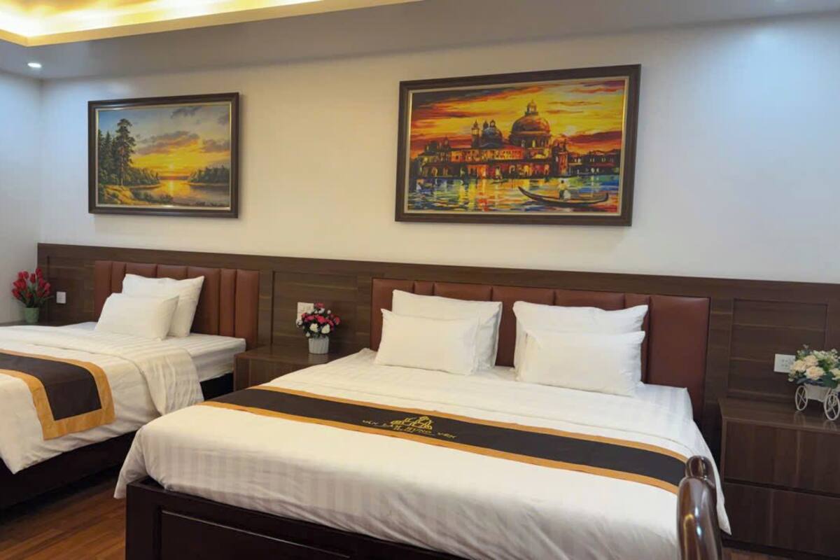 Two double beds with matching headboards, a nightstand with a vase of flowers, and two paintings on the wall.