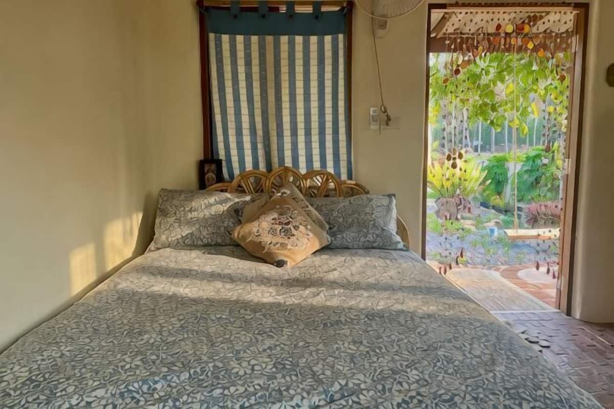 A bed with patterned bedding, a wooden headboard, and a view of a garden through a door.
