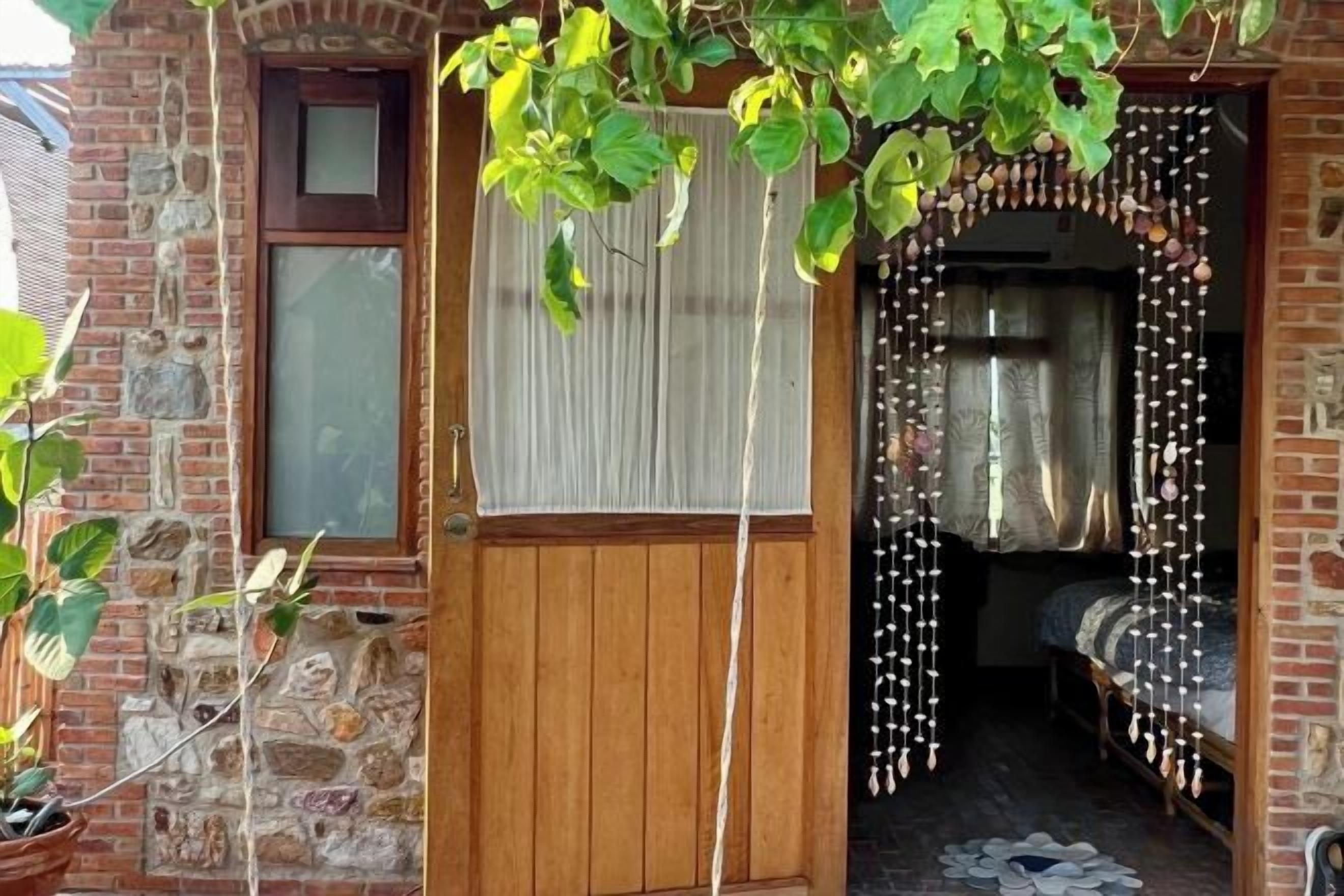 A wooden door with a window, a small room with a bed and curtains, and a stone wall.