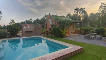 A swimming pool with a brick border, a small brick structure, and a patio area with outdoor furniture.