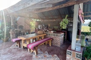 Un patio esterno con angolo barbecue in mattoni, arredi in legno e una panchina decorativa.