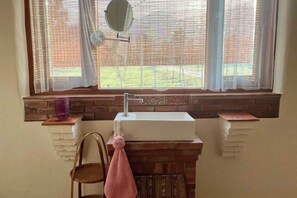 Un baño con lavamanos, espejo y ventana con persianas.