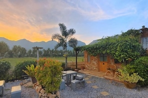 A patio area with outdoor seating, a stone wall, and a view of mountains. - Driftwood & Jolie Cottages (Sam Roi Yot)