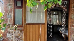 A wooden door with a window, a stone wall, and a room with a bed and curtains.