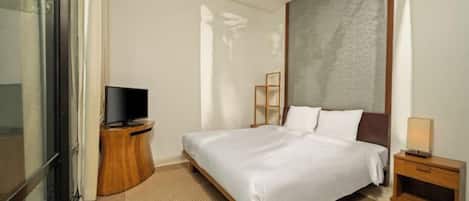 A hotel room with a bed, a television on a wooden side table, a ceiling fan, and a view of the outdoors.