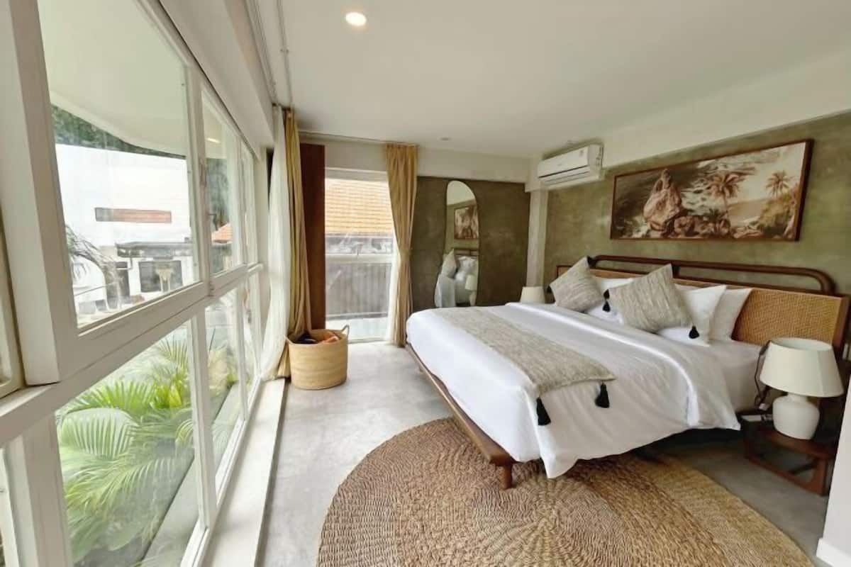 A bedroom with a large bed, a window, and a painting on the wall.
