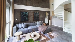 A modern living room with a grey sofa, a round coffee table, and a spiral staircase. - A.K.A Tropicana Bingin Uluwatu (Bali)