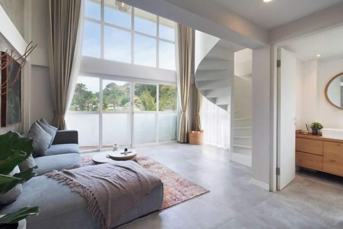 A modern living room with a sofa, a coffee table, and a large window with curtains.