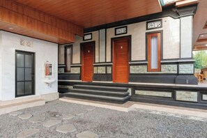 A building entrance with a wooden ceiling, a stone pathway, and three wooden doors. - RedDoorz @ Pondok Kampung Harmony Ubud (Bali)