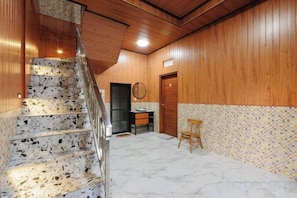 Ein Korridor mit Marmorboden, einer Holztreppe, einer Holztür und einem kleinen Hocker.