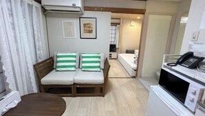 A compact room with a sofa, a small table, a microwave, and an air conditioning unit. - MTOKYO (Tokyo)