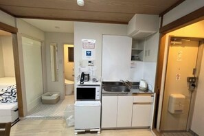 A compact hotel room with a kitchenette, a bed, a small bathroom, and a door leading to another room. - MTOKYO (Tokyo)