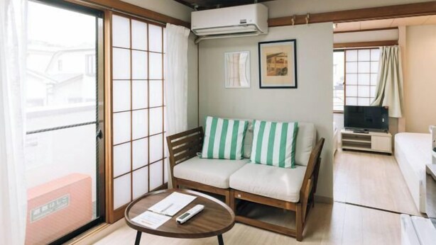 A traditional Japanese-style room with tatami flooring, a low wooden table, a sofa with green and white cushions, a television on a stand, and a sliding glass door. - MTOKYO (Tokyo)