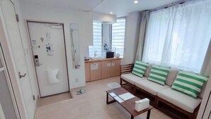 A modern living room with a sofa, a coffee table, a kitchen area, and a door. - MTOKYO (Tokyo)