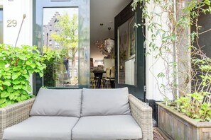 Ein Korbusofa mit Kissen in einem Innenhof mit Blick auf ein Gebäude und eine Straße.