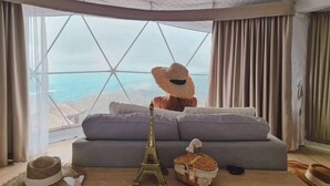 A cozy living room with a large window, a sofa, a bear-shaped cushion, a model of the Eiffel Tower, and a basket of bread. - Thenor (Samoeng)