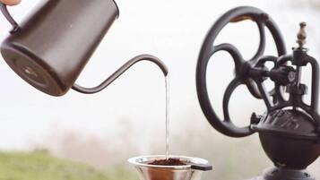 A hand pouring liquid from a metal pitcher into a coffee dripper over a coffee machine.