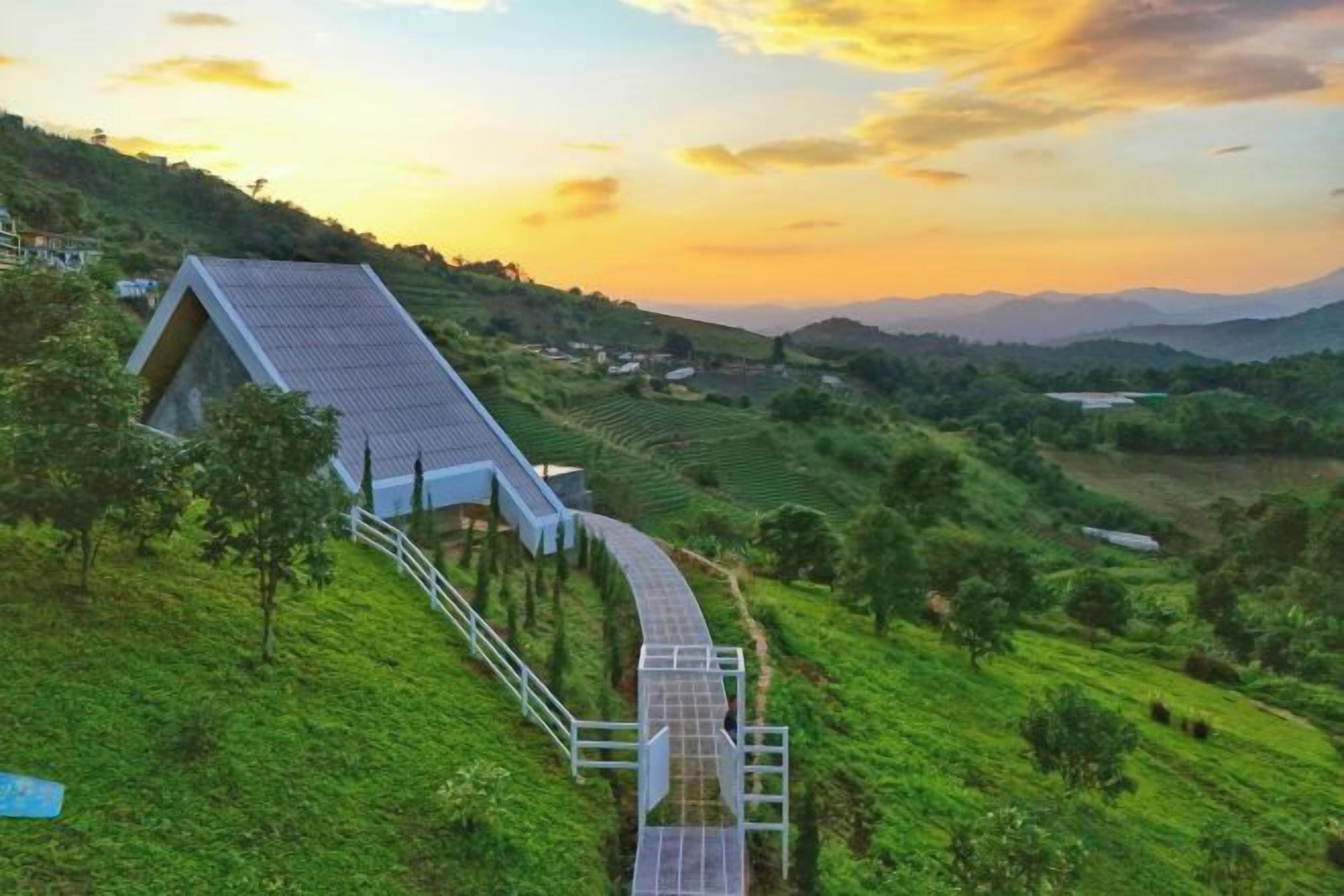 A modern building with a sloped roof, surrounded by lush green fields and a winding pathway leading to it.
