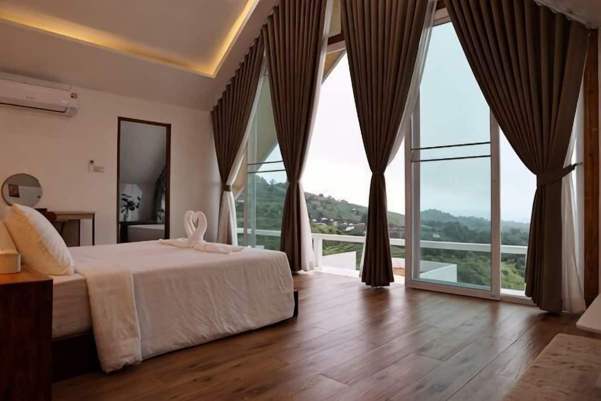 A bedroom with a large bed, a bedside table, a mirror, and a view through floor-to-ceiling windows.