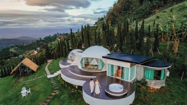 A modern, circular building with a glass facade, surrounded by lush greenery and a scenic view. - Thenor (Samoeng)