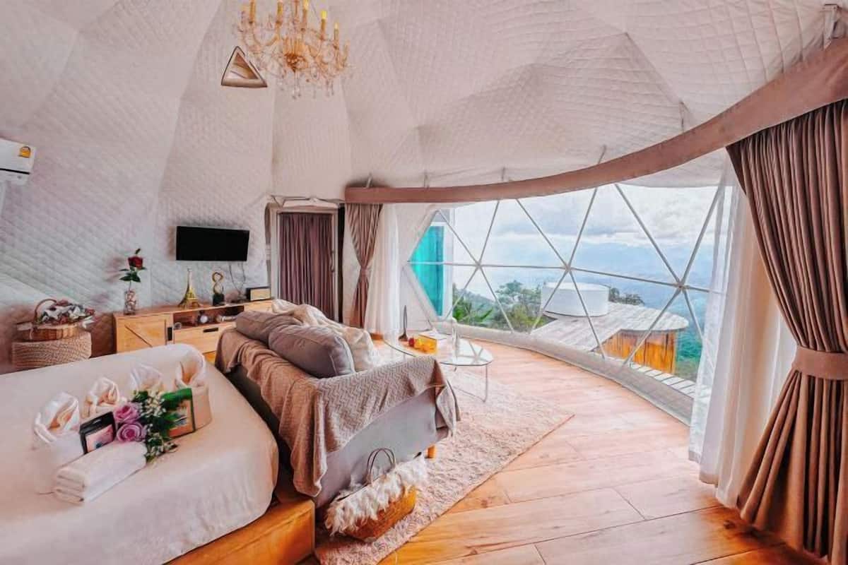 A spacious room with a bed, a TV, a window with a view, and a chandelier.