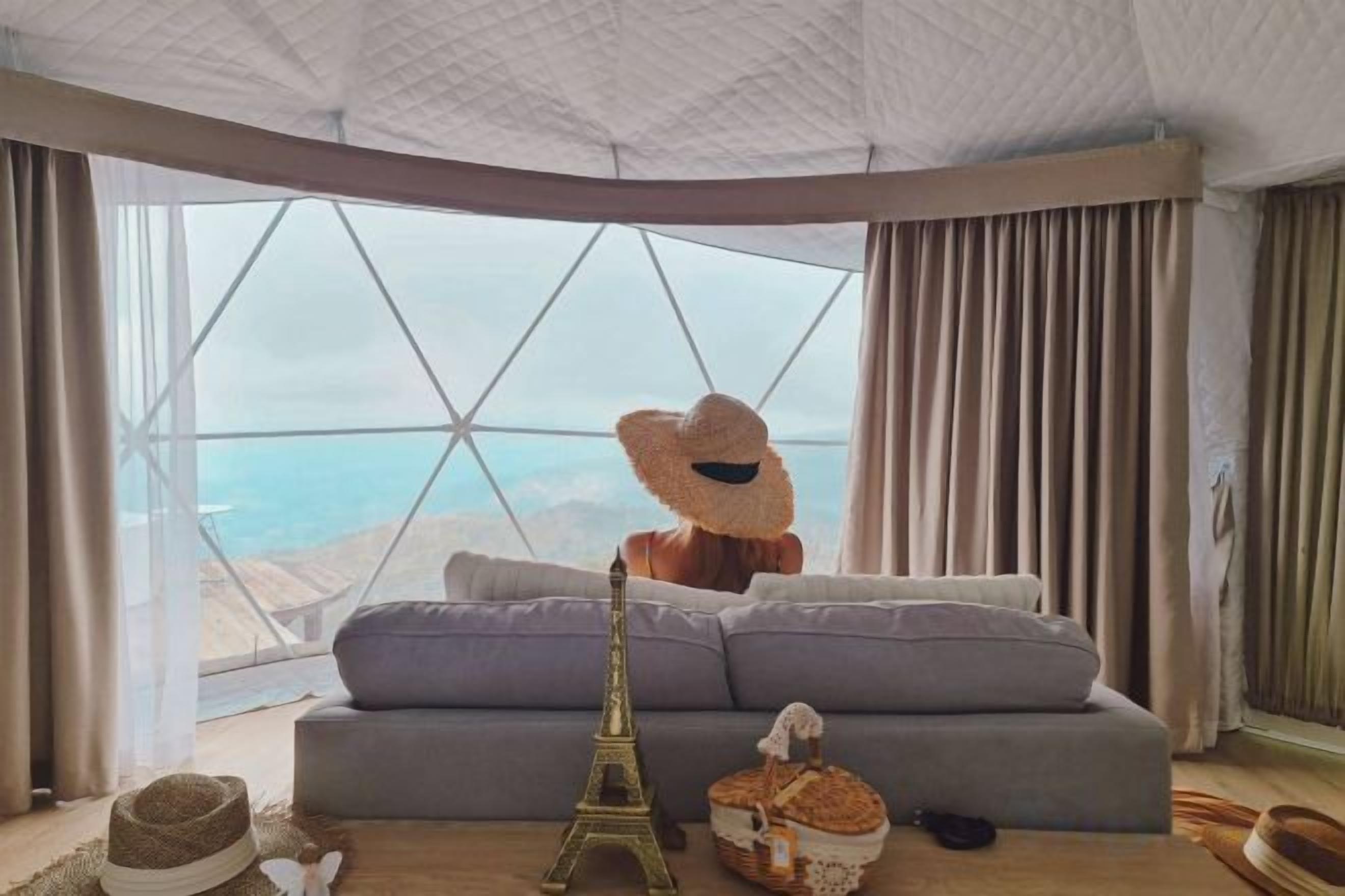 A room with a large window, a sofa, a decorative hat, and a small Eiffel Tower model.
