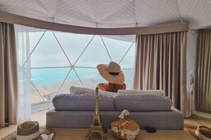 A room with a large window, a sofa, a decorative hat, and a small Eiffel Tower model. - Thenor (Samoeng)