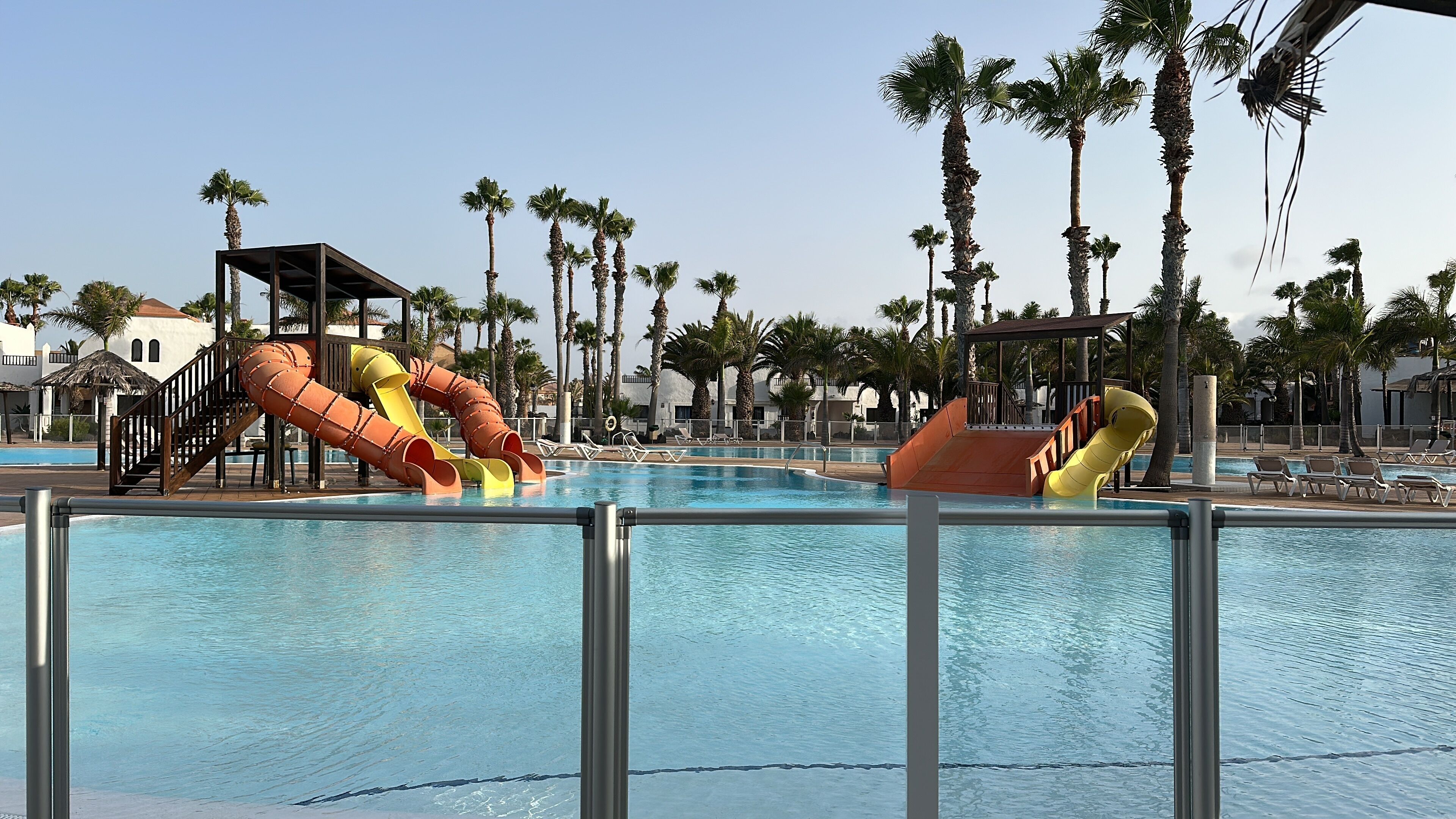 A swimming pool with two water slides, palm trees, and lounge chairs.