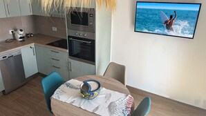 Una cocina moderna con electrodomésticos de acero inoxidable, una mesa de comedor con un mantel decorativo y un televisor de pantalla plana mostrando a un surfista.
