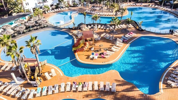 Un resort con varias piscinas, zonas de descanso y palmeras.