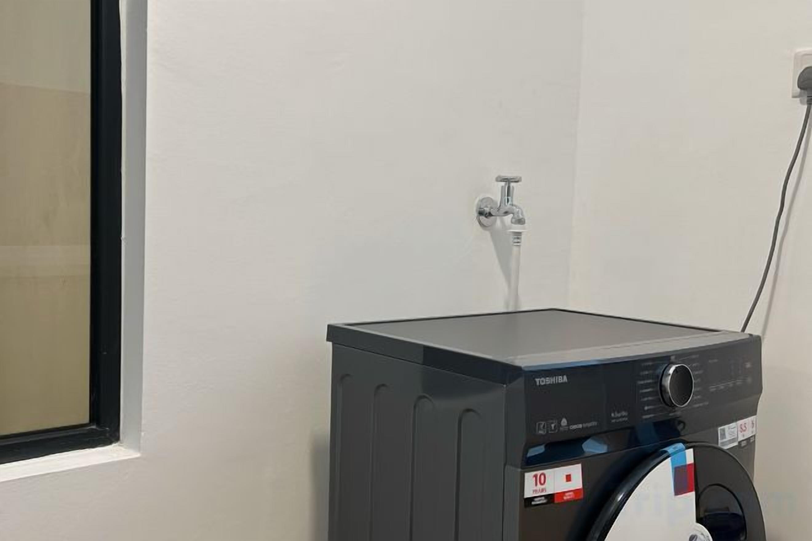 Máquina de lavar compacta e escura num quarto com parede branca e janela.