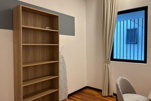 A room with a wooden bookshelf, a window with a view of a blue sky, and a chair. - Jelutong Luxe Stay (Shah Alam)
