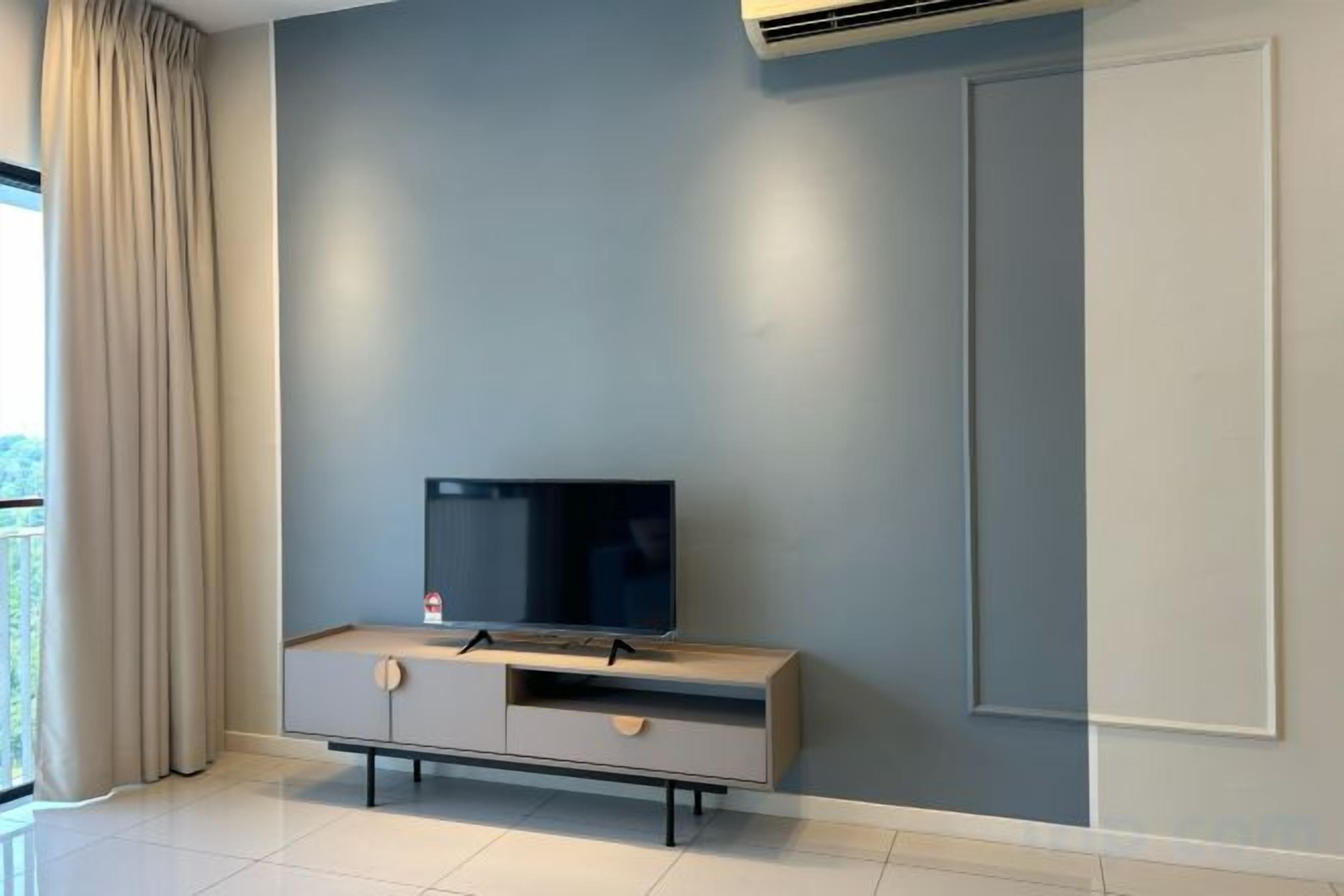 A modern living room with a flat-screen TV on a grey cabinet, a large window with curtains, and a white door.