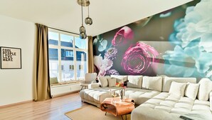 Una sala de estar moderna con un amplio sofá modular, una mesa de centro de madera y vistas de la ciudad a través de grandes ventanales.