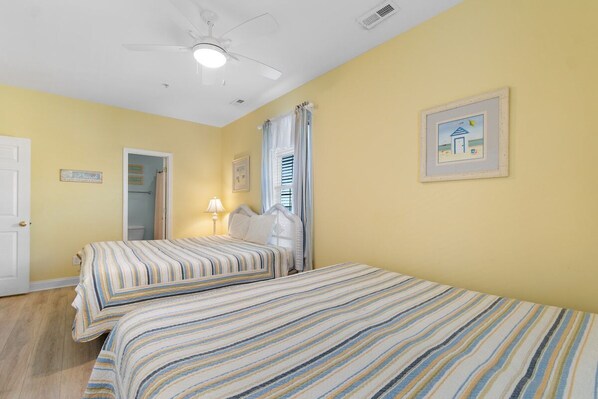 A room with two beds, a ceiling fan, a door, and a framed picture on the wall.