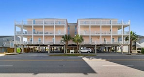 A two-story building with a flat roof, multiple balconies, and a parking area in front.