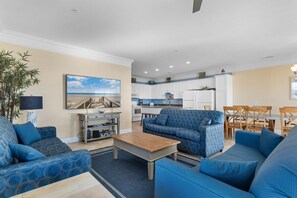 A living room with blue patterned sofas, a wooden coffee table, and a painting of a beach scene.