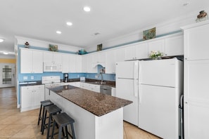 A modern kitchen with white cabinets, a granite countertop, and a central island with bar stools.