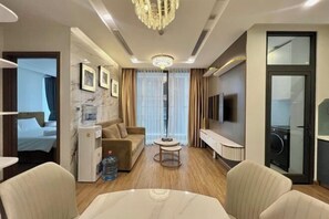 A hotel room with a bed, a sofa, a TV, a coffee table, and a minibar. - Vinhome Metropolis Luxury Apartment - Tiramisu House (Hanoi)