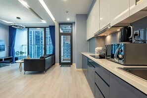 A modern kitchen with stainless steel appliances, a black sofa, and a view of a cityscape through large windows. - Vinhome Metropolis Luxury Apartment - Tiramisu House (Hanoi)