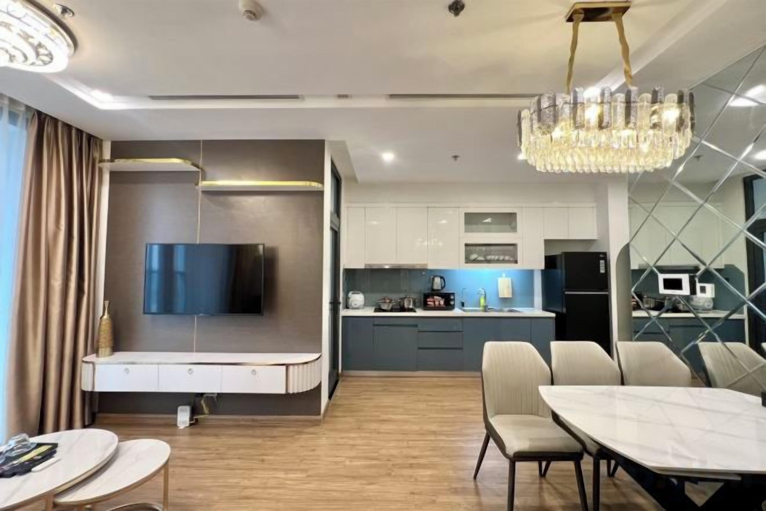 Una sala moderna con un televisor de pantalla plana, un comedor con mesa de mármol y una cocina al fondo.