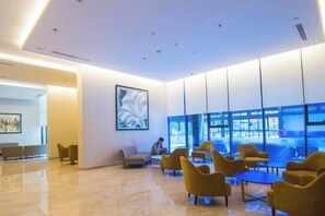 A modern lobby with seating areas, a large abstract painting, and a glass wall with a view. - Vinhome Metropolis Luxury Apartment - Tiramisu House (Hanoi)