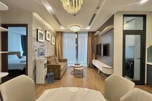 A hotel room with a bed, a sofa, a TV, a coffee table, and a minibar. - Vinhome Metropolis Luxury Apartment - Tiramisu House (Hanoi)