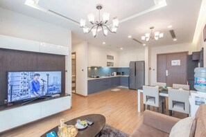 A modern living room with a flat-screen TV, a dining area with a table and chairs, and a kitchen in the background. - Vinhome Metropolis Luxury Apartment - Tiramisu House (Hanoi)