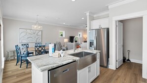 Una cucina moderna con lavastoviglie integrata, elettrodomestici in acciaio inossidabile e un'area pranzo con sedie blu e un piano di lavoro in marmo.