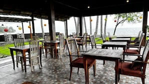 An outdoor dining area with wooden tables and chairs, a tiled floor, and a view of the sea.